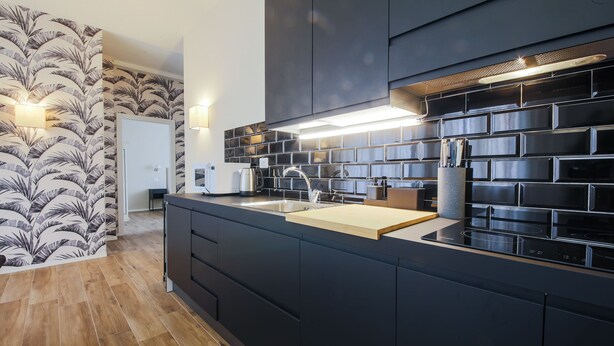 A modern kitchen with dark cabinetry, a wooden countertop, and a backsplash with a geometric pattern. - Apartments Florence - Novella Bloom (Florence)