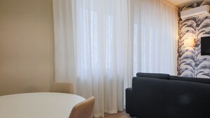 A room with a round table, a black sofa, and a wall-mounted air conditioner. - Apartments Florence - Novella Bloom (Florence)