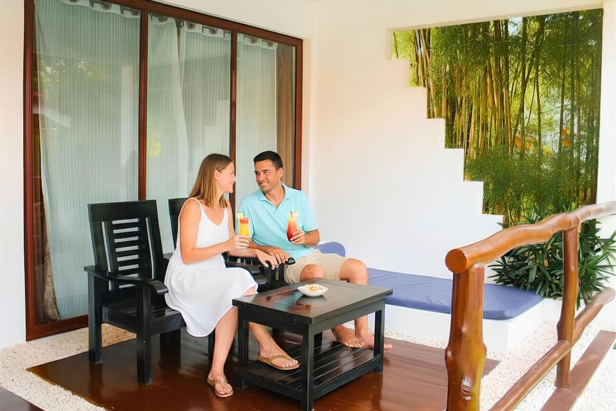 Un couple est assis sur un balcon d’où l’on peut admirer une forêt de bambous, une balustrade en bois et une petite table sur laquelle sont posées des boissons.
