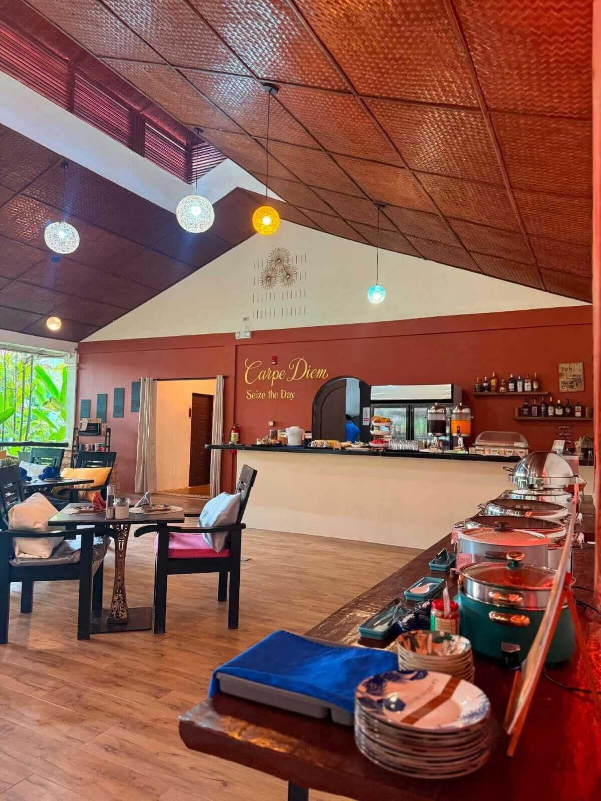 A restaurant with a high ceiling, a buffet area with various dishes, and a sign that reads 'Carpe Diem Seize the Day.'