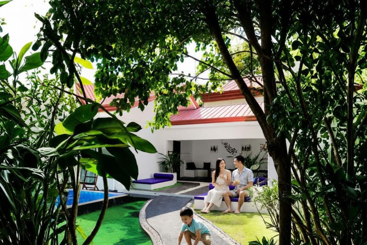 Une famille avec un enfant sur un skateboard, dans un espace aménagé avec une piscine et un bâtiment doté d’un toit rouge.