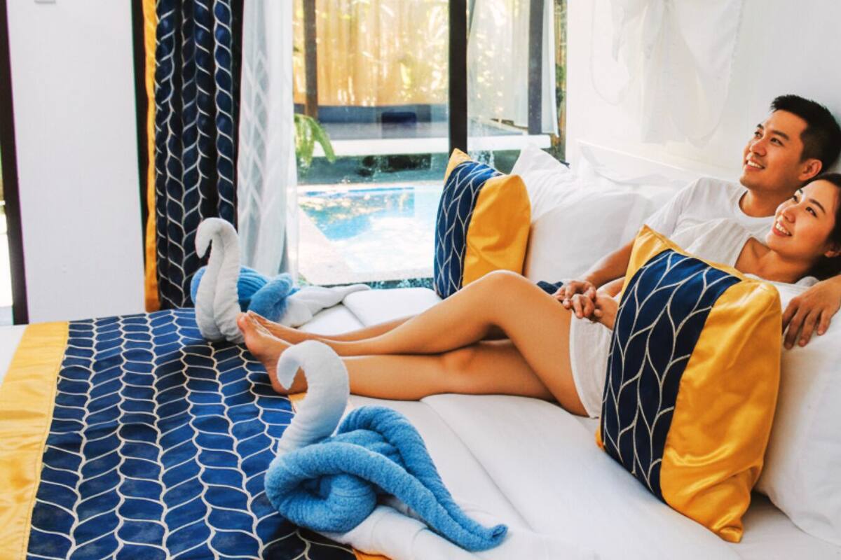 Un couple est allongé sur un lit recouvert d’une couvre-lit à motifs, avec des oreillers et une couverture.