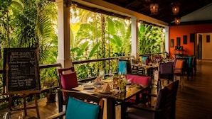 Un restaurant intérieur avec des tables dressées pour le service, un menu écrit à la craie et une végétation luxuriante visible à travers de grandes fenêtres.