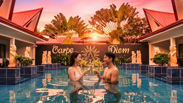 Un couple dans une piscine, avec un coucher de soleil en arrière-plan, entouré de plantes tropicales et de statues.