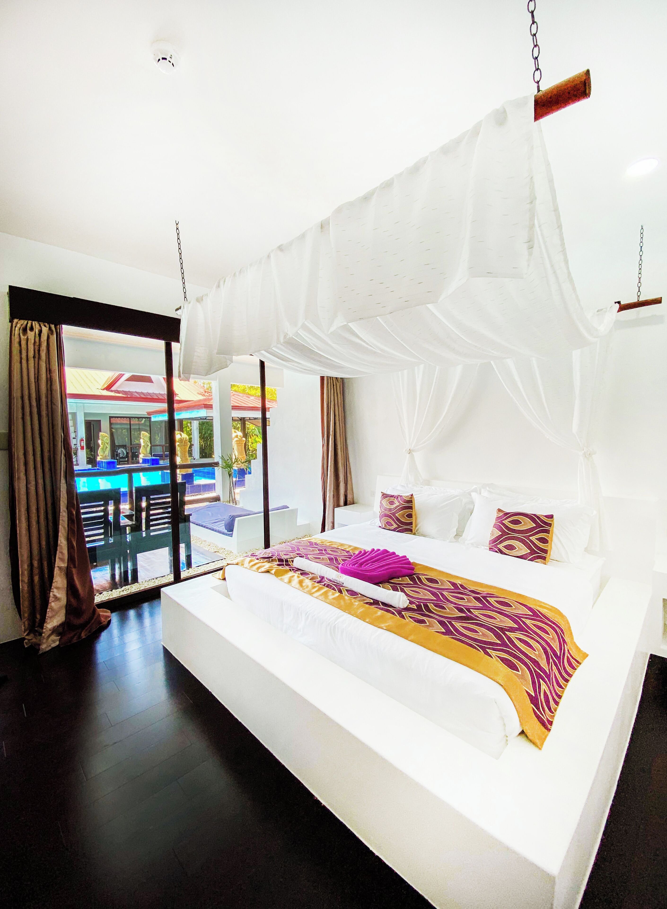 A spacious bedroom with a large bed, white canopy, and a view of an outdoor pool area.