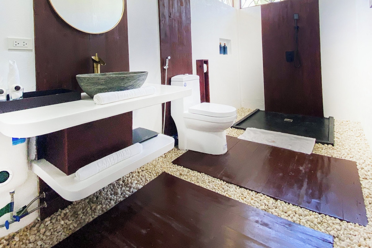 Une salle de bain avec un grand miroir, un lavabo avec un receveur, des toilettes et un espace douche.