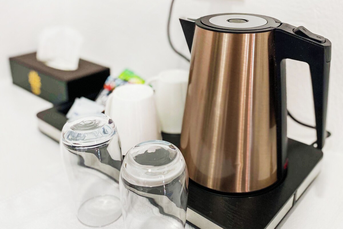 A coffee maker on a black stand with a white countertop, a tissue box, and two glasses.