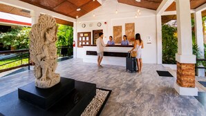 Un espace d’accueil comprenant un comptoir de réception, une statue et un autre comptoir de réception où travaillent trois employés.