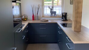 A modern kitchen with dark cabinetry, a wooden ceiling, and a window with a decorative deer. - New charming half-timbered house by the lake in the idyllic Münsterland region (Warendorf)