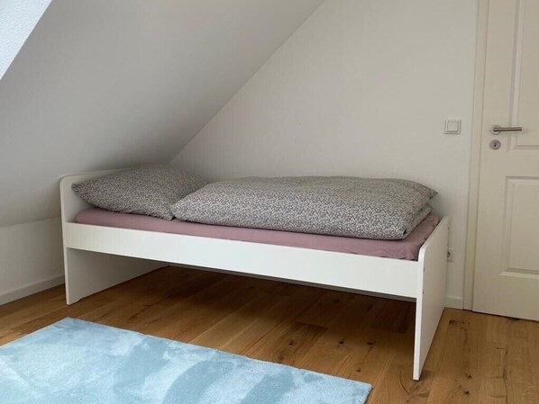 Una cama litera blanca con dos almohadas, un tapete azul claro y suelo de madera.