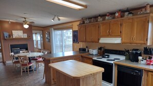 A kitchen with wooden cabinets, a stove, a dishwasher, and a dining area with chairs and a table. - Cabin Getaway! (Remer)