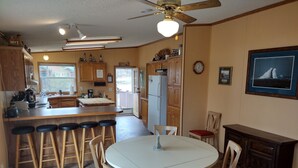 A kitchen with a central island, wooden bar stools, a dining table with chairs, and a ceiling fan. - Cabin Getaway! (Remer)