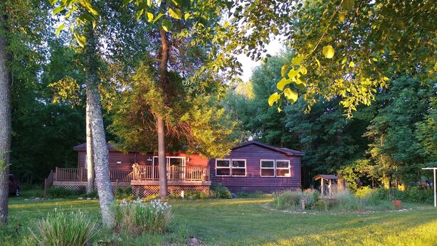 A cabin with a deck, surrounded by trees and a grassy yard. - Cabin Getaway! (Remer)