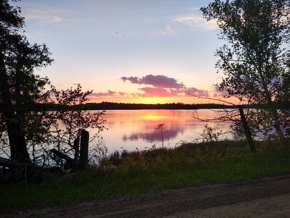 A serene lakeside view with a sunset, surrounded by trees and a dirt path. - Cabin Getaway! (Remer)