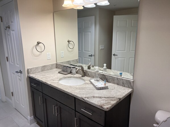 A bathroom with a marble countertop, a sink, a mirror, and a toilet.