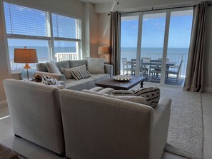 A modern living room with a sofa, two armchairs, a coffee table, and a view of the ocean through large windows.