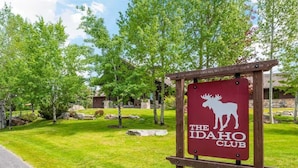 Un cartell del The Idaho Club amb un logo de mufló, envoltat de vegetació i un camí pavimentat.