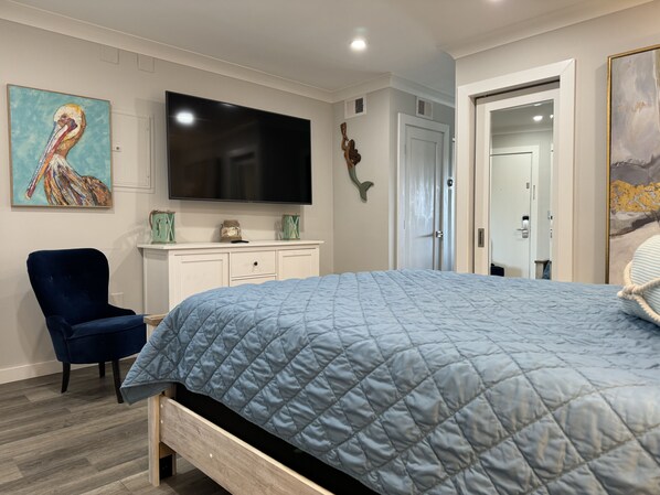 A bedroom with a bed, a TV, a chair, and artwork on the walls.