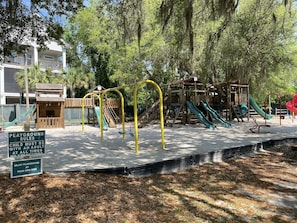 Children can play on the swings and slides in this playground area surrounded by trees.