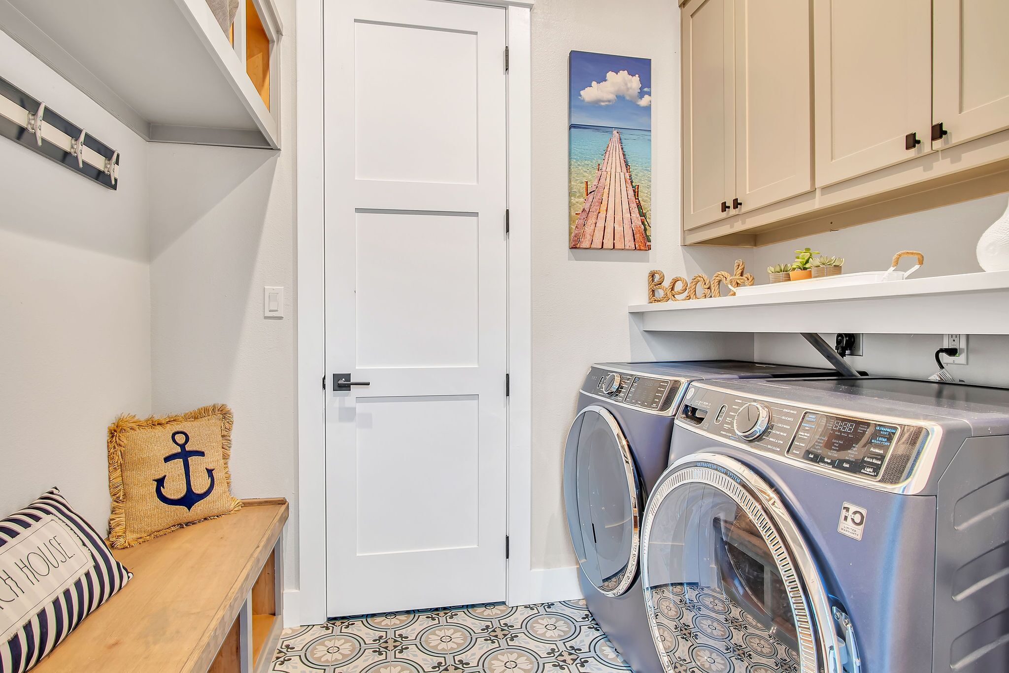 A laundry room with a washing machine, a bench with a pillow, a door, and a wall with a painting.