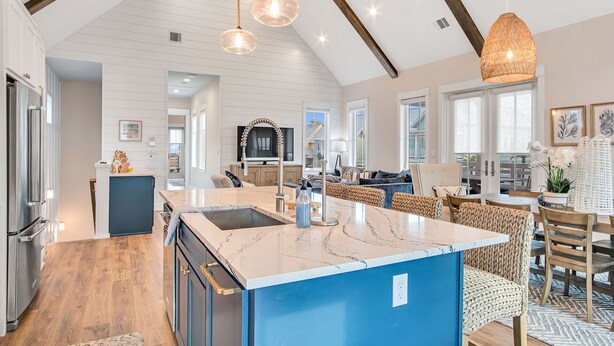 Une cuisine spacieuse avec un îlot central bleu, un plancher en bois et des luminaires suspendus.