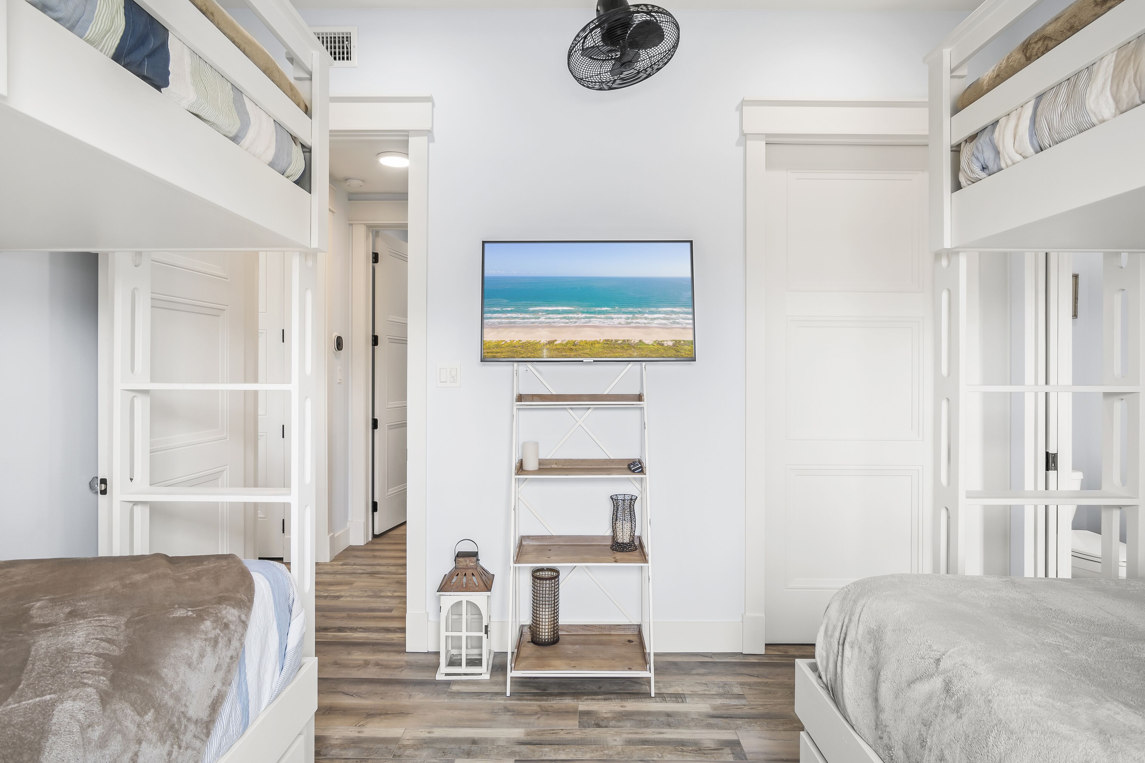 A bedroom with a TV mounted on the wall, a wooden floor, and a bunk bed.