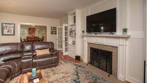 Ein Wohnzimmer mit Ledersofa, Flachbildfernseher, Kamin und Essbereich im Hintergrund.