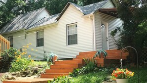 Ein Haus mit Veranda, einer Treppe aus Holz zum Eingang und einem Garten mit verschiedenen Pflanzen und Blumen.