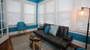 Una sala de estar con un sofá de cuero negro, un sillón azul y una pequeña mesa de madera.