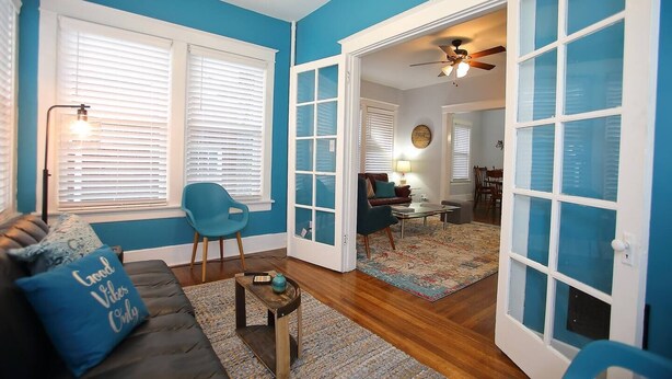 Un salón con pared azul, un sofá oscuro con un cojín, una mesita de centro de madera y una silla azul.