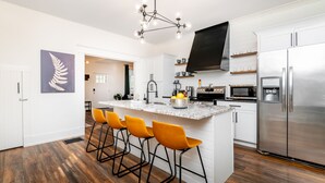 A modern kitchen with a central island, bar stools, a stainless steel refrigerator, and a pendant light.