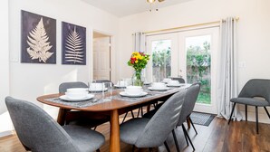 A dining area with a wooden table set for six, grey upholstered chairs, and a vase of flowers.