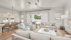 A spacious living room with a dining area, a ceiling fan, and large windows.
