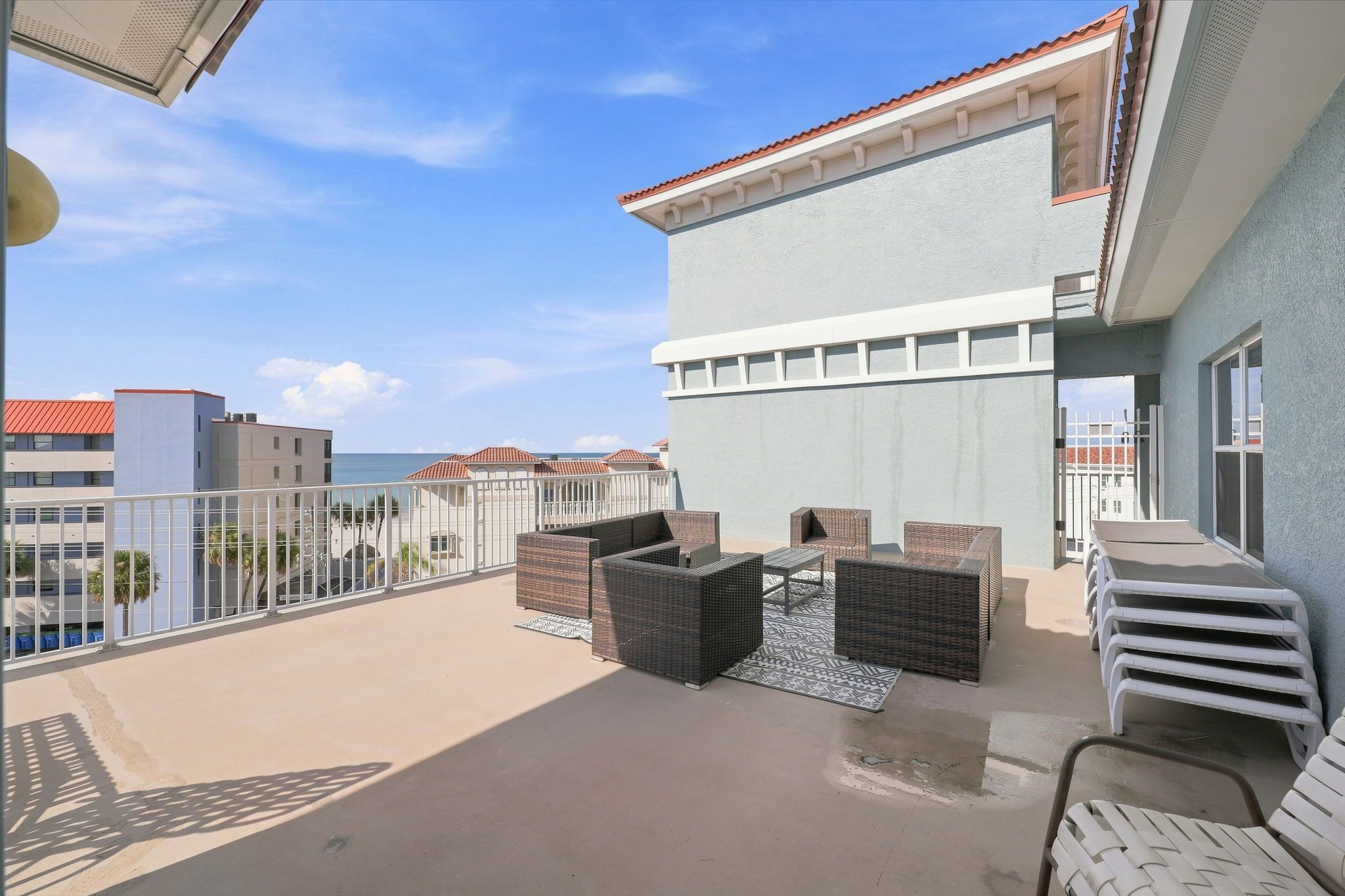 Un balcon agrémenté de meubles en osier, une vue sur l’océan et un bâtiment avec un toit rouge.