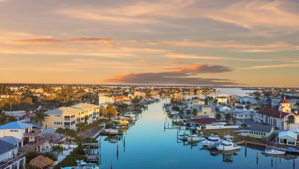 Un puerto deportivo con barcos amarrados, rodeado de edificios residenciales y una vía fluvial tranquila.