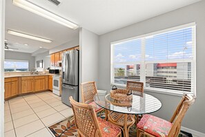 A modern kitchen with stainless steel appliances, a dining area with wicker chairs, and a large window with blinds.