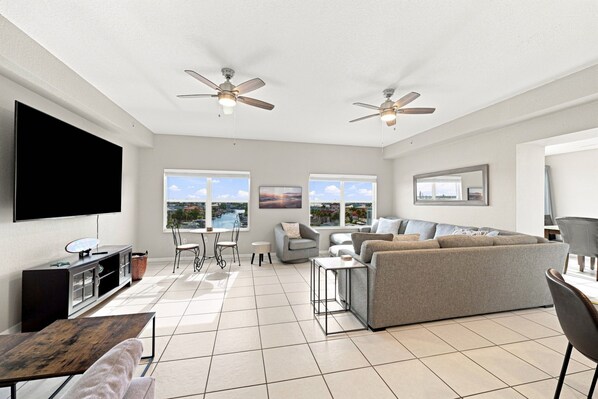 A spacious living area with a flat-screen TV, two ceiling fans, a grey sofa, a coffee table, and a TV stand. - Penthouse condo with amazing views! Private 1000 sf balcony (Madeira Beach)