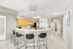 A modern kitchen with wooden cabinets, a central island with bar stools, and recessed ceiling lights.