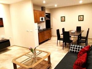 A compact living space with a dining area, kitchenette, and a glass-top coffee table with a vase.