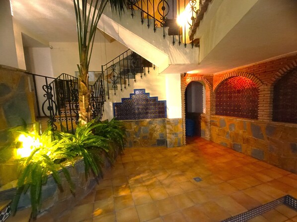 Un espacio interior amplio con una escalera, paredes de piedra y suelo de baldosas.