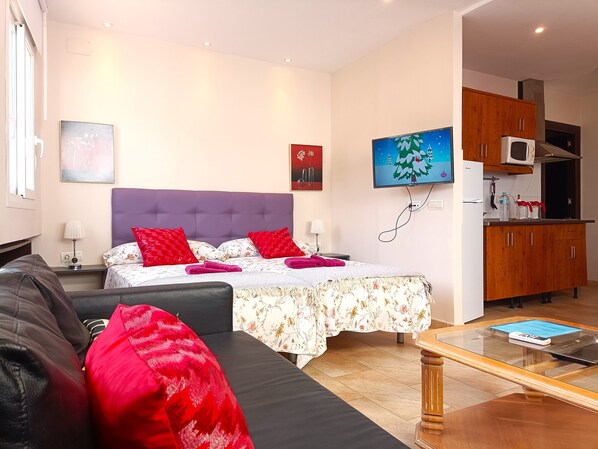 Une chambre moderne avec un grand lit, un canapé, une table basse et un coin cuisine doté de meubles en bois et d’un four à micro-ondes.
