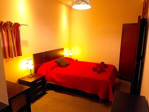 A bedroom with a red bedspread, two bedside lamps, a wooden nightstand, and a headboard.