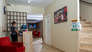 Un vestíbulo de hotel con mostrador de recepción, sillas rojas, un cuadro en la pared y una escalera.