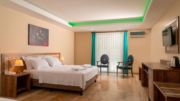Habitación de hotel con cama, mesita de noche con lámpara, escritorio con silla, televisión y ventana con cortinas.