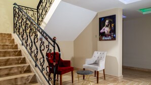 Una escalera con barandales negros ornamentados, una silla roja, una silla blanca y una pequeña mesa redonda con tapa de mármol.