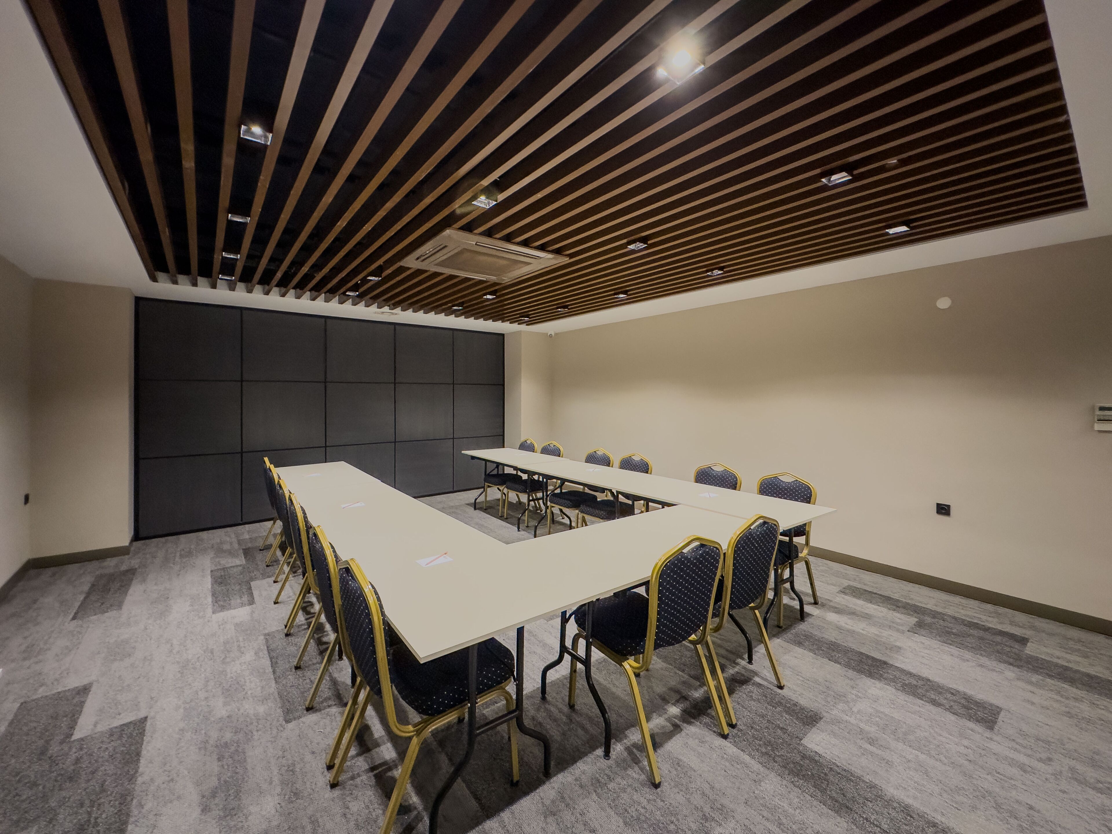 Un salón de conferencias con una larga mesa, sillas y un diseño de techo moderno.