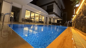 A swimming pool with clear blue water, surrounded by a modern building with large windows and outdoor seating. - Quality Gold Suit Hotel (Antalya)