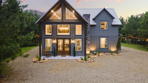 A modern two-story house with a stone facade, large windows, and a gravel driveway. - Broken Bow Secluded Playset Retreat for Families (Broken Bow)