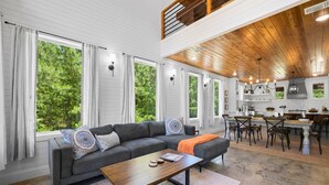A modern living room with a sectional sofa, a coffee table, and a dining area with a kitchen in the background. - Broken Bow Secluded Playset Retreat for Families (Broken Bow)