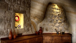 A rustic stone interior with a wooden cabinet, a window with a red object, and a stone wall.
